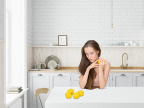 Mujer joven sentada en la cocina y sosteniendo limón