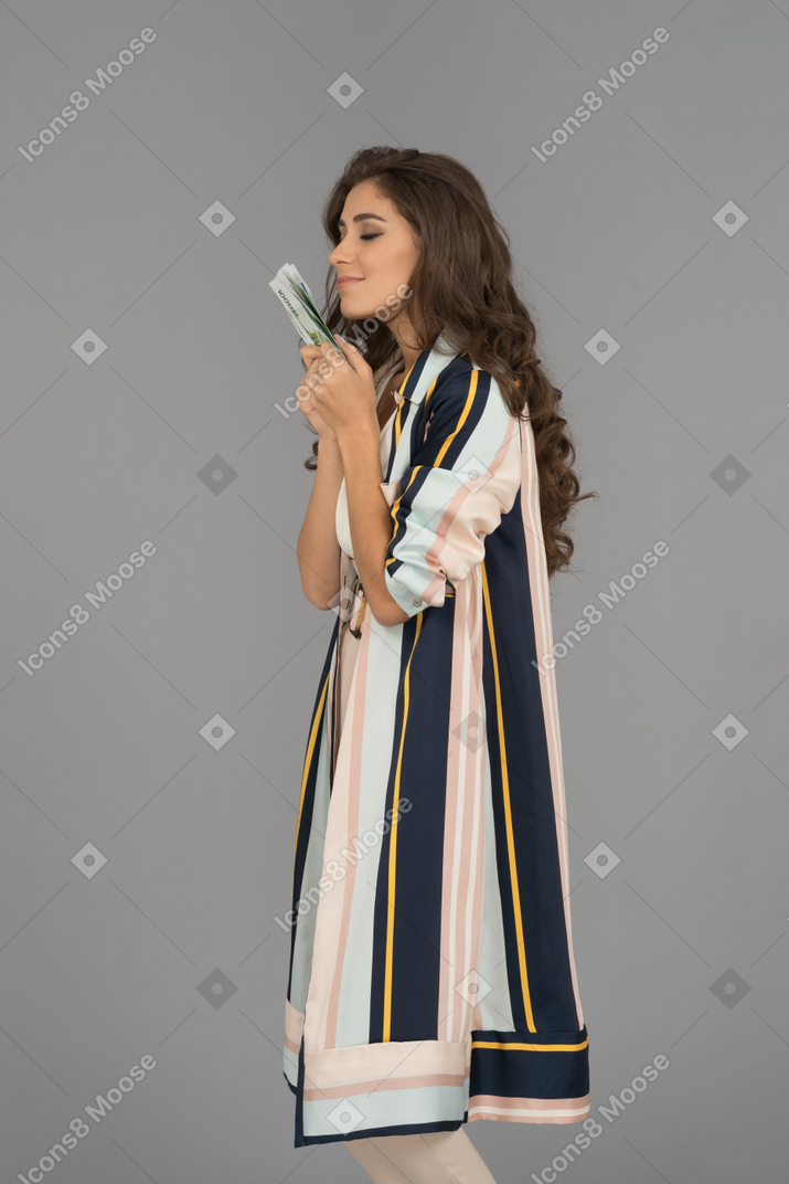 Красивая молодая женщина, наслаждаясь запахом банкнот