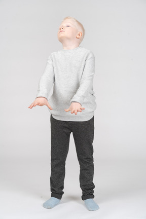 Vista frontal de un niño rubio extendiendo los brazos y levantando la cabeza
