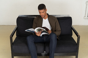 Beau jeune homme assis sur un canapé et tenant un magazine