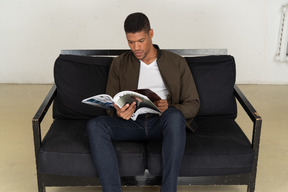 Beautiful young man sitting on a sofa and holding a magazine