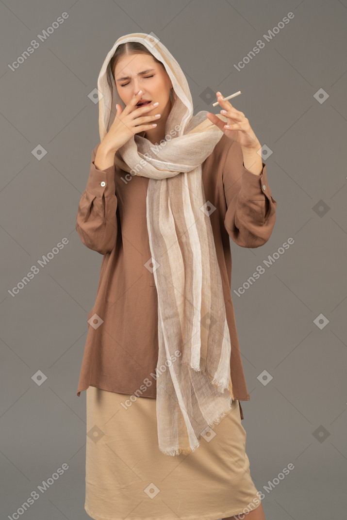 Young woman in headscarf coughing from cigarette
