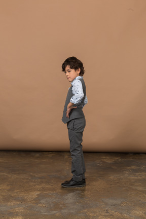 Vista lateral de un niño con traje gris de pie con las manos en las caderas