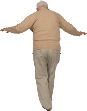 Rear view of an old man in casual clothes walking with outstretched arms