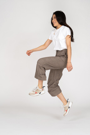 Vista lateral de uma jovem saltitante de calça e camiseta levantando a perna