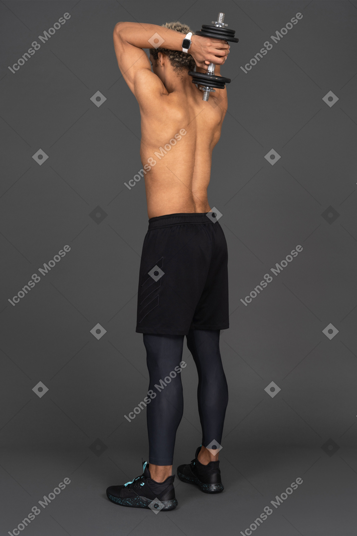 Vista traseira de três quartos de um homem afro sem camisa levantando o haltere