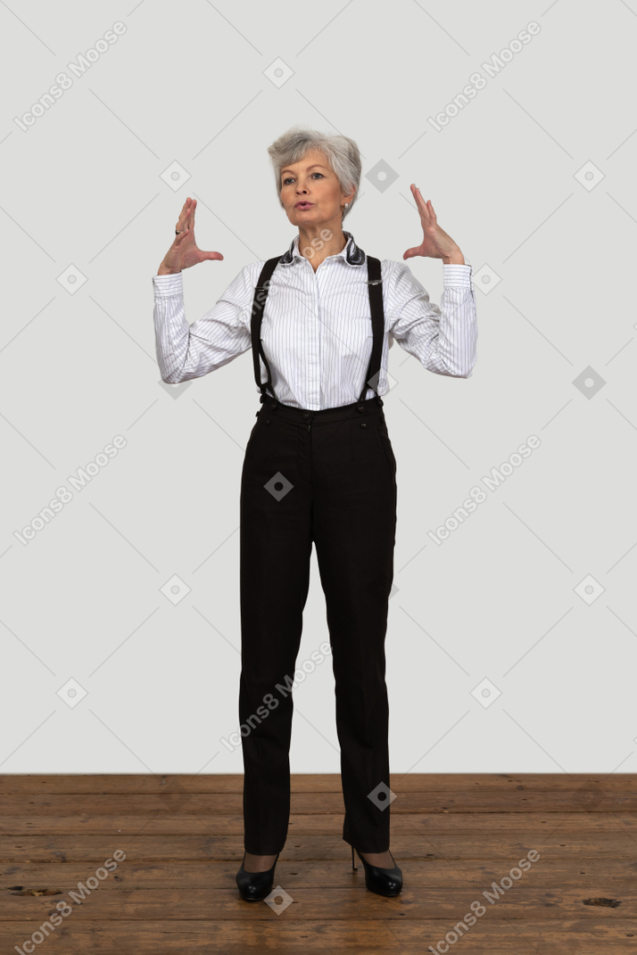 Vista frontal de una anciana en ropa de oficina gesticulando activamente de pie en la habitación
