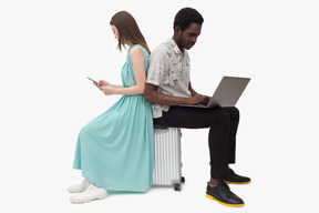 Interracial couple sitting on suitcase and and using gadjets