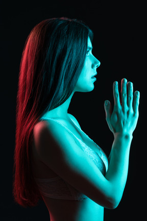 Portrait de profil d'une femme en sous-vêtements mettant les mains sous la lumière bleue