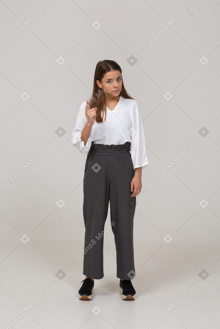 Front view of a warning young lady in office clothing raising finger