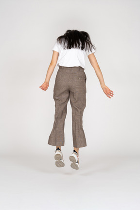 Vista traseira de uma jovem saltitante de calça e camiseta olhando para baixo