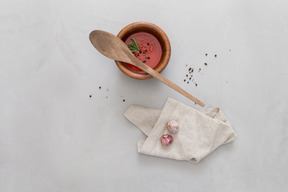 A bowl of gazpacho, some garlic and wooden spoon