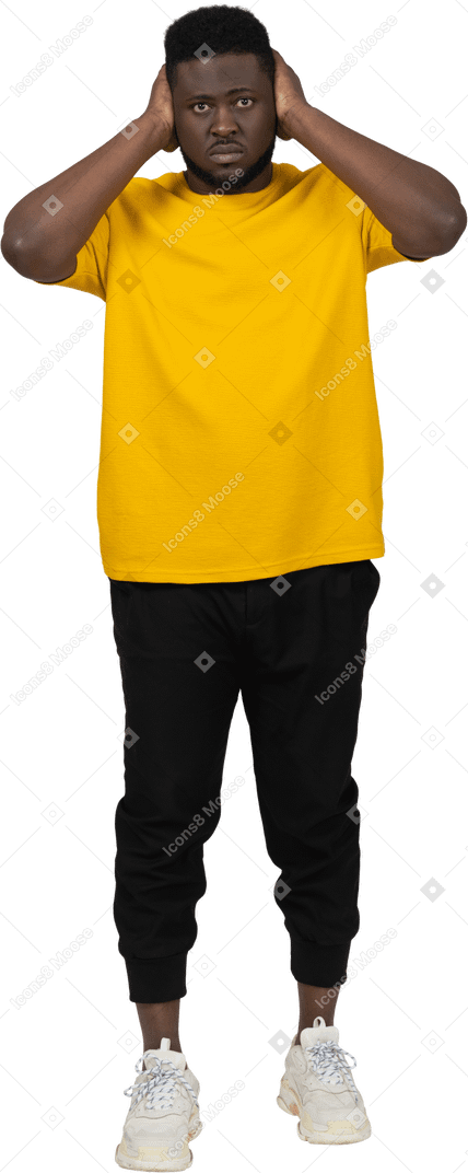 Vista frontal de un hombre de piel oscura con camiseta amarilla bloqueando sus oídos