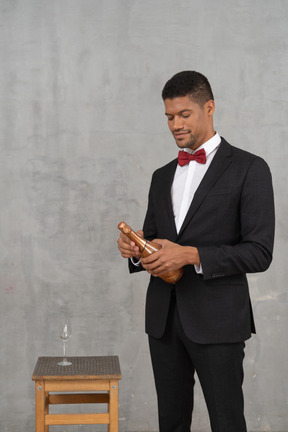 Мужчина в костюме и галстуке-бабочке стоит с бутылкой шампанского