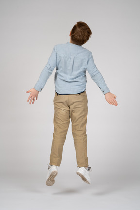Back view of a boy in casual clothes jumping with his arms outstretched