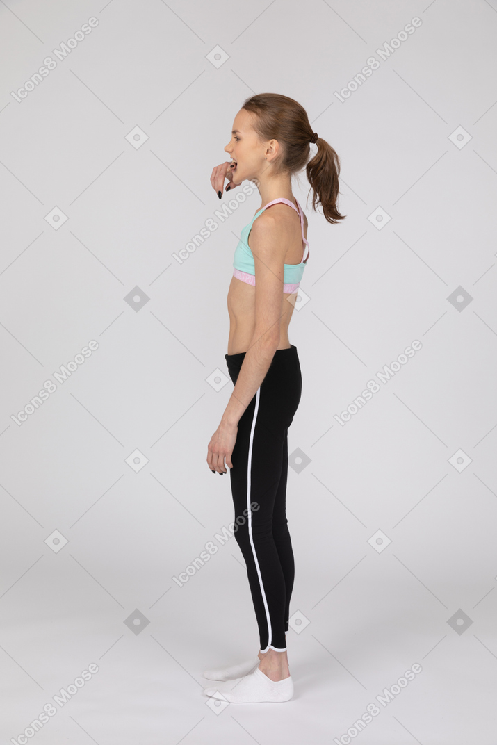 Vista lateral de una jovencita en ropa deportiva mordiendo su dedo