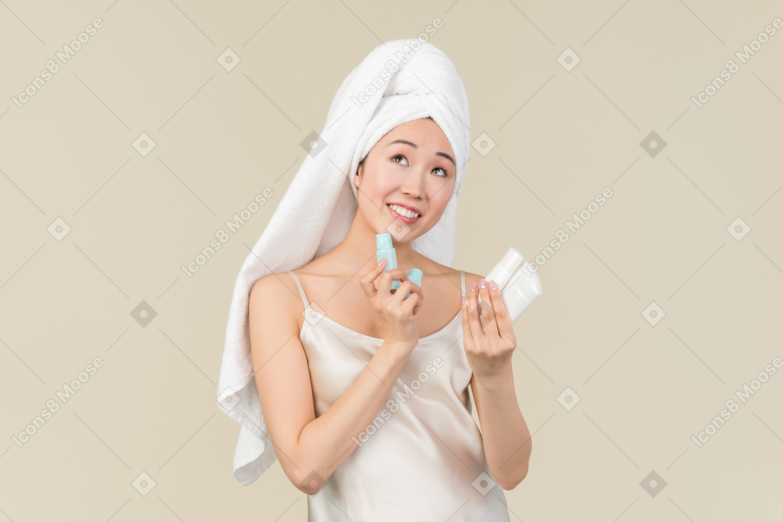 Young asian woman with hair wrapped in towel holding beauty products