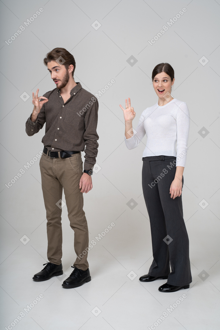 Трехчетвертный вид молодой пары в офисной одежде, показывающей знак ок