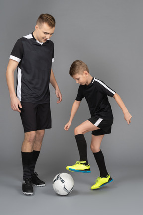 De cuerpo entero de un joven entrenando a un niño pequeño cómo jugar fooyball