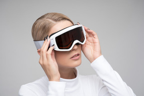 Young woman in white turtleneck adjusting ski goggles