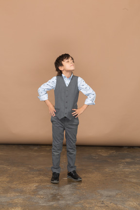 Vue de face d'un garçon en costume gris posant avec les mains sur les hanches