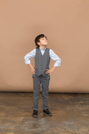 Vista frontal de un niño con traje gris posando con las manos en las caderas