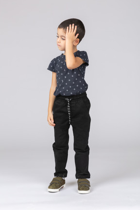 Vista frontal de un niño en ropa casual de pie con las manos en la cabeza.