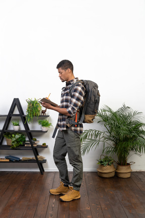 Side view of a tourist with a backpack writing down in his notepad