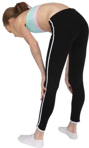 Vista posterior de tres cuartos de una jovencita en ropa deportiva inclinada hacia adelante y tocando las piernas