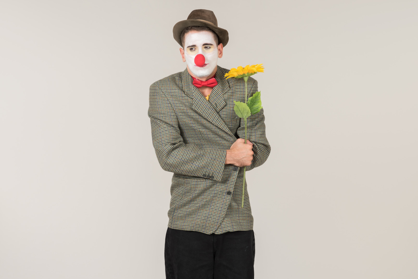 Sad looking male clown holding sunflower