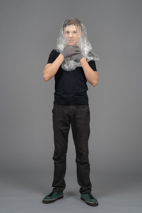 Male model on neutral background chokes himself with plastic wrap