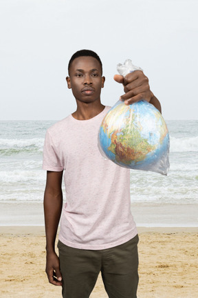 A man standing on a beach holding an earth globe model in a plastic bag