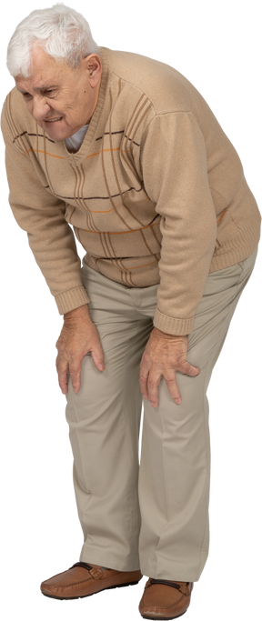 Vue de face d'un vieil homme en vêtements décontractés se penchant et touchant ses genoux blessés