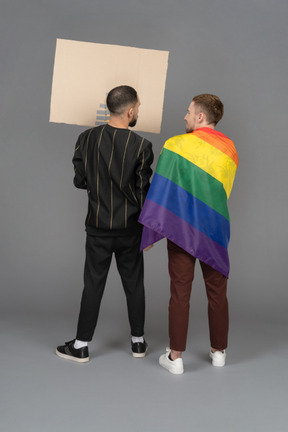 Rückansicht von zwei jungen männern mit einer plakatwand und einer lgbt-flagge