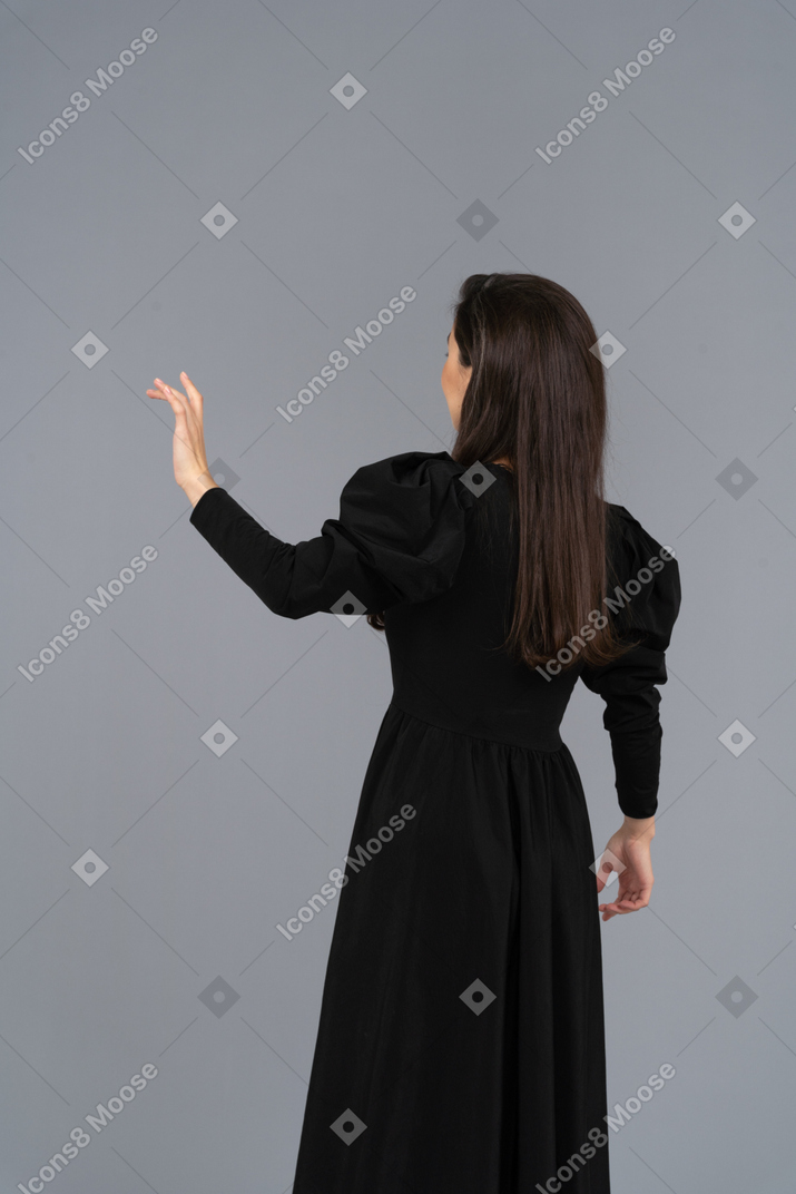 Вид сзади молодой леди в черном платье, поднимающей руку