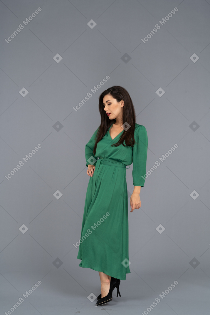 Vue de trois quarts d'une jolie jeune femme en robe verte mettant la main sur la hanche