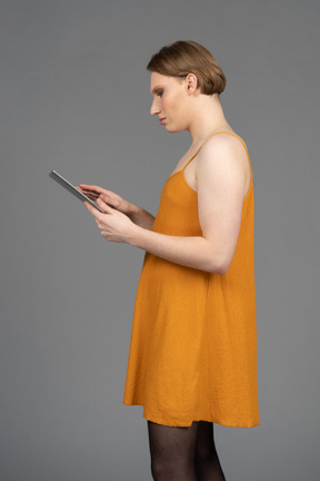 Jeune transgenre en robe orange à l'aide d'une tablette numérique