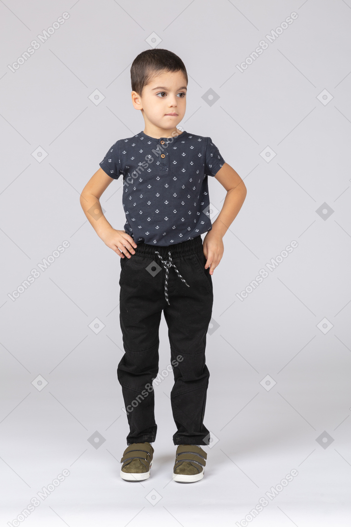 Front view of a cute boy in casual clothes posing with hands on hips
