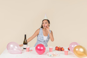 Молодая азиатская девушка сидит за столом на день рождения и свистит