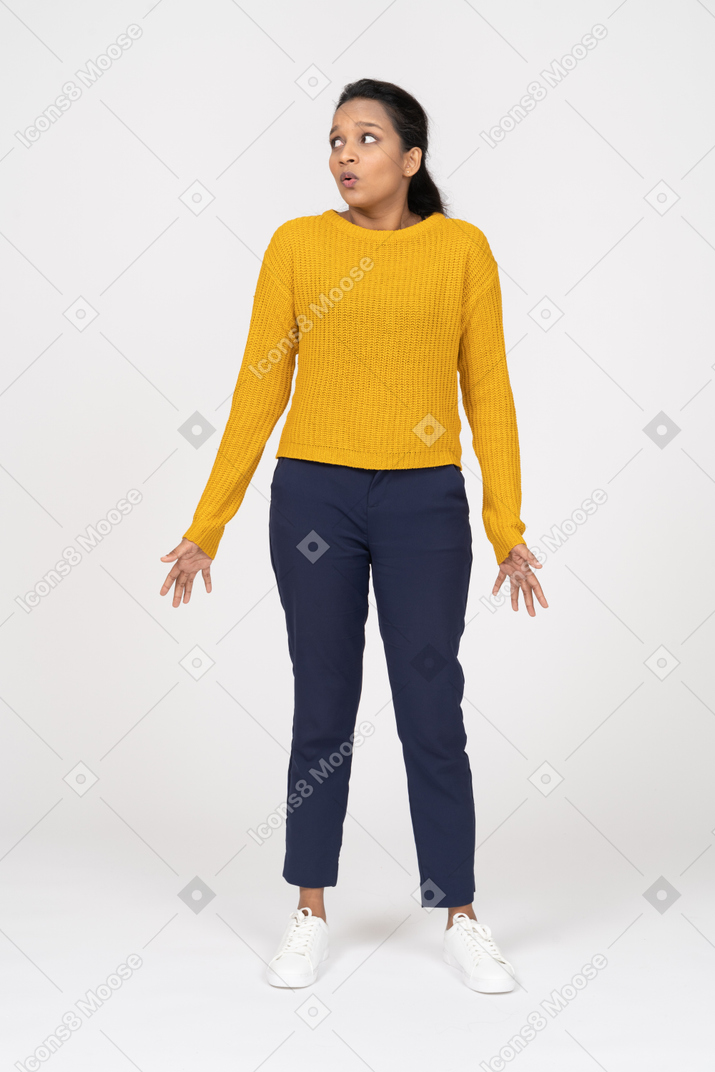 Vista frontal de una chica confundida en ropa casual de pie con los brazos extendidos