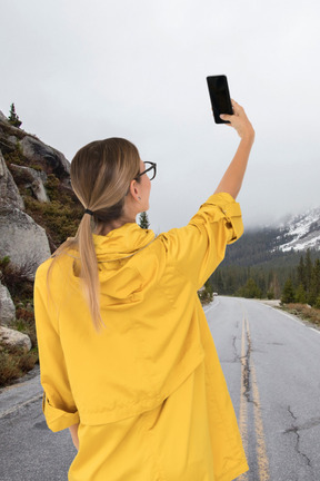 A woman in a yellow raincoat taking a picture with her phone