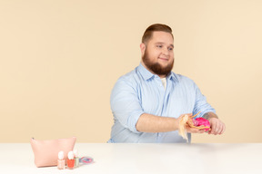 Sorridente timido giovane grande uomo seduto al tavolo e in possesso di barbie doll