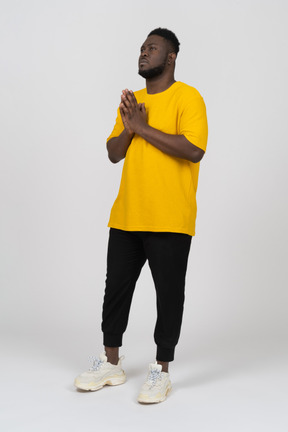 Three-quarter view of a young dark-skinned man in yellow t-shirt holding hands together