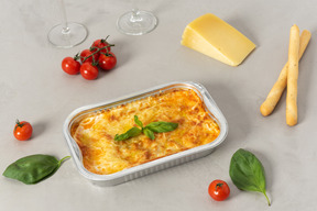 Stück lasagne, käse, kirschtomaten, grissini und gläser