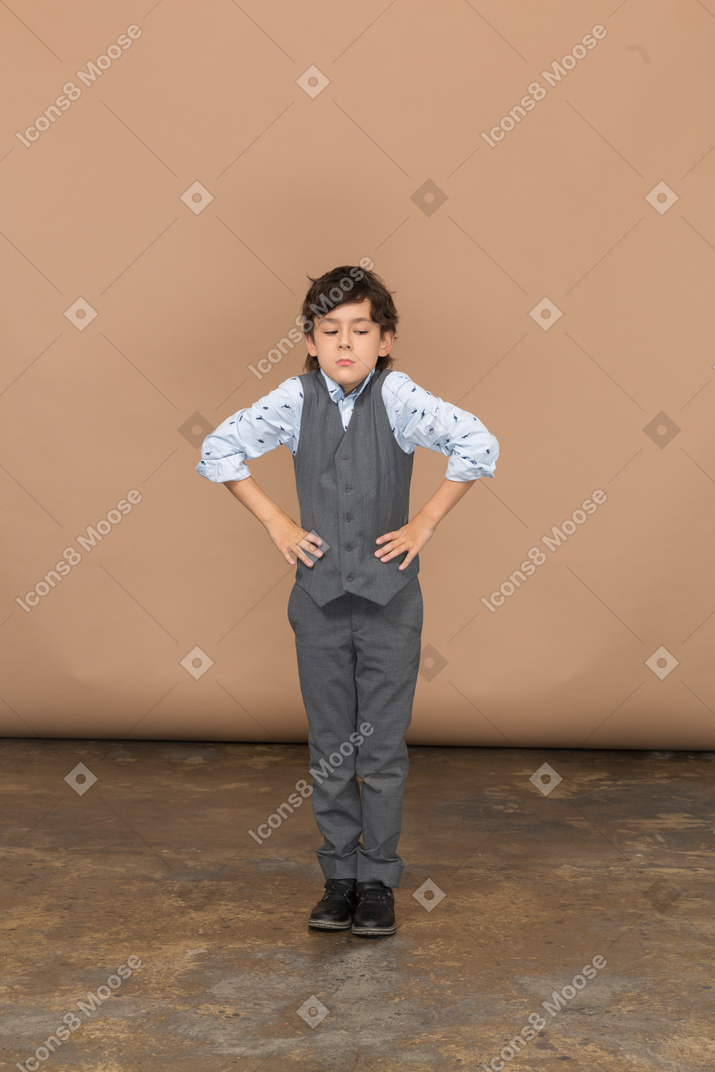 Front view of a cute boy in grey suit posing with hands on hips