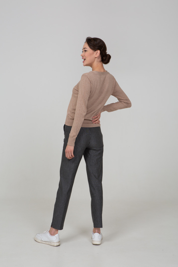 Three-quarter back view of a laughing female in pullover and pants putting hand on hip