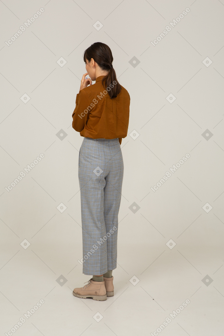 Three-quarter back view of a young asian female in breeches and blouse touching mouth
