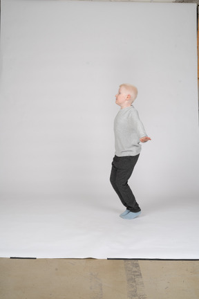Vista lateral de un niño de pie con las rodillas dobladas y los brazos extendidos
