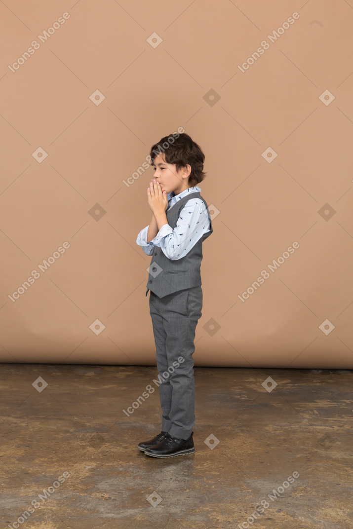 Vista lateral de um menino de terno fazendo gesto de oração
