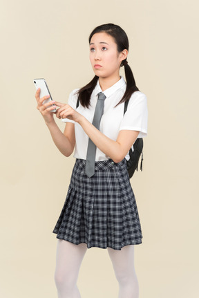 Involved in thoughts asian school girl holding smartphone